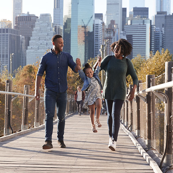 Mom and Dad each hold their young daughter by hand as the family crosses a pedestrian bridge